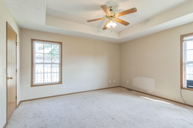 unfurnished room with ceiling fan, a raised ceiling, and plenty of natural light