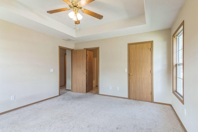 unfurnished bedroom with a raised ceiling, light colored carpet, and ceiling fan