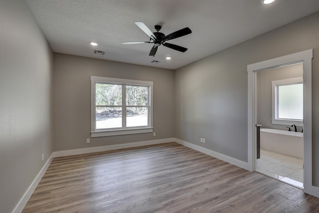 empty room featuring ceiling fan, a healthy amount of sunlight, a textured ceiling, and light hardwood / wood-style flooring