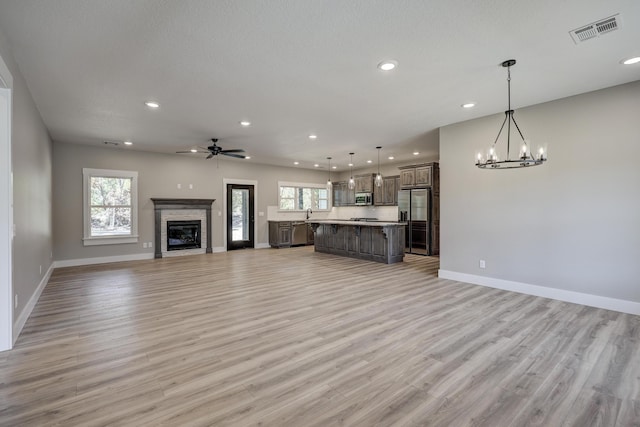 unfurnished living room with light hardwood / wood-style floors, a textured ceiling, and ceiling fan with notable chandelier