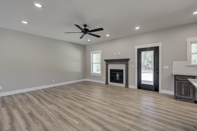 unfurnished living room featuring a wealth of natural light, a fireplace, light wood-type flooring, and ceiling fan