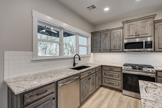 kitchen with tasteful backsplash, appliances with stainless steel finishes, sink, light stone counters, and light hardwood / wood-style flooring