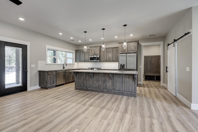 kitchen with stainless steel appliances, a center island, a barn door, pendant lighting, and light hardwood / wood-style floors