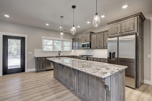 kitchen featuring a kitchen island, a kitchen bar, decorative light fixtures, light wood-type flooring, and appliances with stainless steel finishes