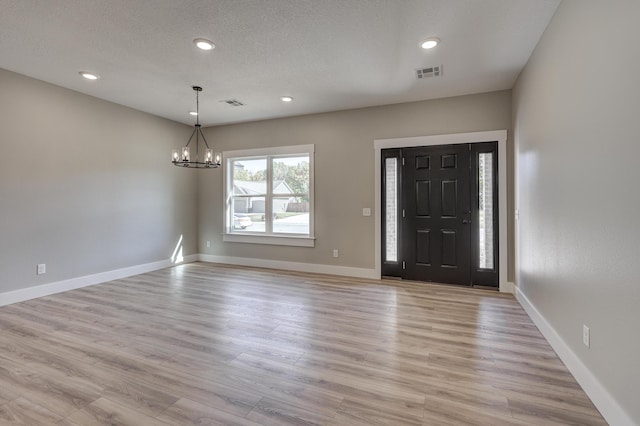 entrance foyer with light hardwood / wood-style floors, a notable chandelier, and a textured ceiling