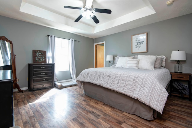 bedroom featuring ceiling fan, dark hardwood / wood-style flooring, and a tray ceiling