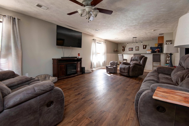 living room with a fireplace, a textured ceiling, ceiling fan, and dark hardwood / wood-style floors