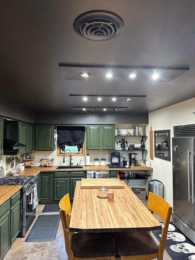 kitchen with sink, green cabinetry, wall chimney range hood, stainless steel appliances, and wood counters