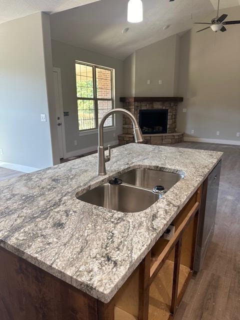 kitchen with lofted ceiling, sink, light stone counters, a center island with sink, and a brick fireplace