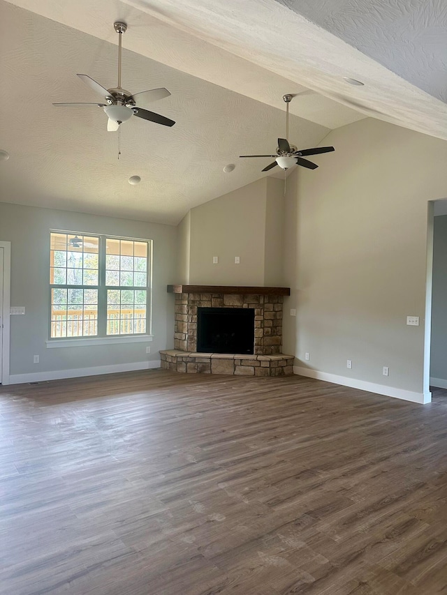 unfurnished living room with ceiling fan, a stone fireplace, dark hardwood / wood-style floors, and a textured ceiling