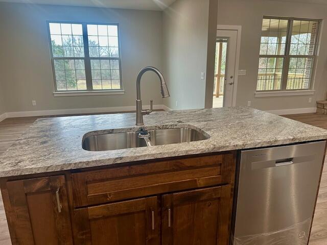 kitchen with plenty of natural light, sink, stainless steel dishwasher, and light stone counters