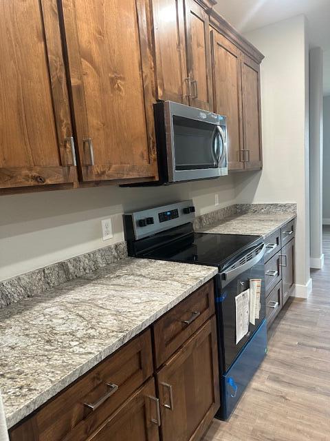 kitchen featuring light stone countertops, electric range oven, and light hardwood / wood-style flooring