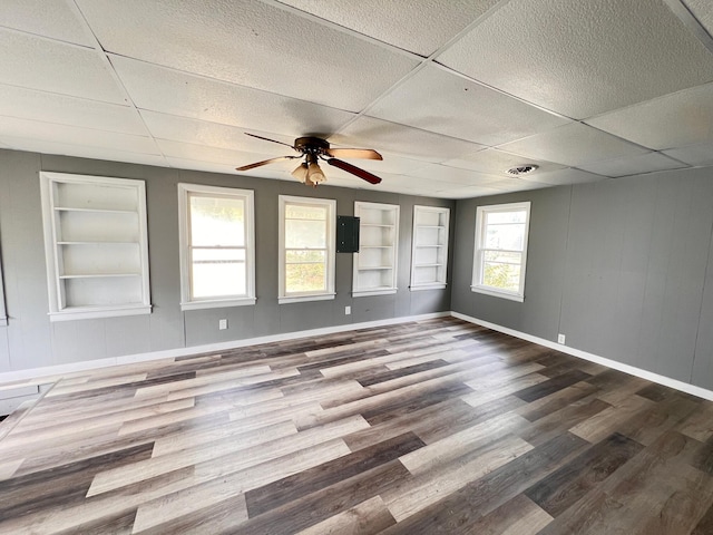 unfurnished room with ceiling fan, hardwood / wood-style flooring, built in features, and a drop ceiling