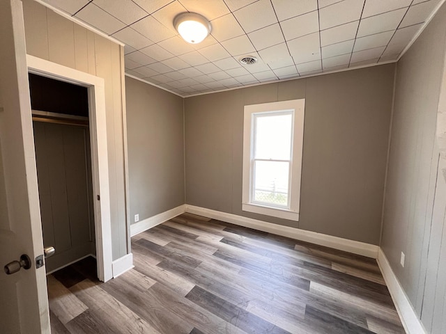 unfurnished bedroom with crown molding, wooden walls, a closet, and wood-type flooring