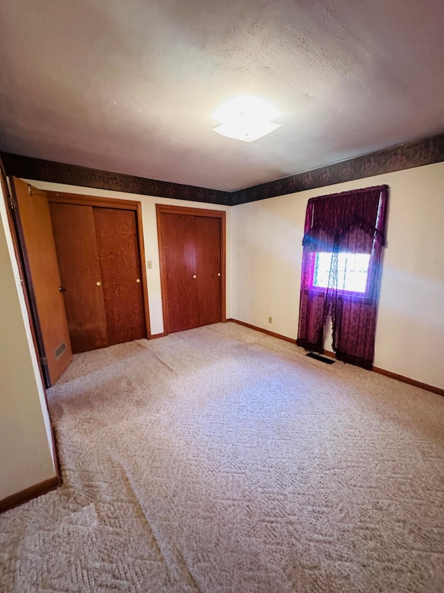 unfurnished bedroom featuring a textured ceiling, light colored carpet, and multiple closets