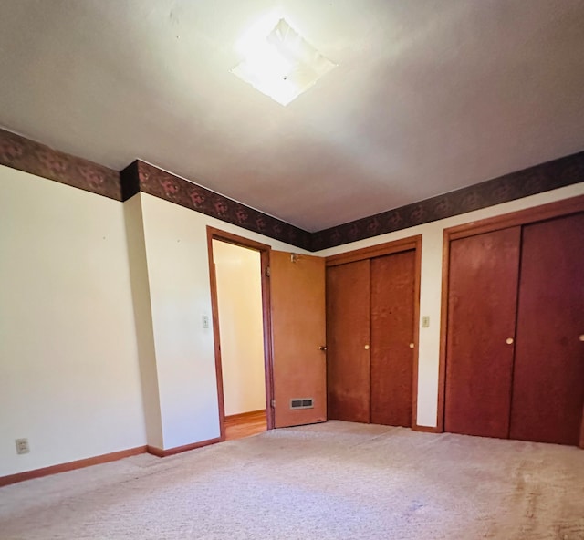 unfurnished bedroom with light colored carpet and multiple closets