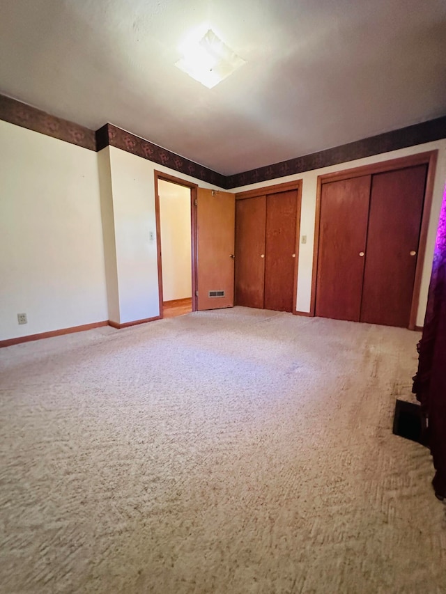 unfurnished bedroom with light colored carpet and two closets