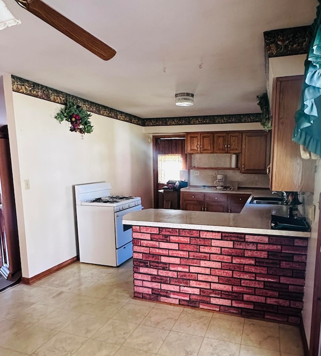 kitchen featuring kitchen peninsula, backsplash, white range with gas cooktop, and sink