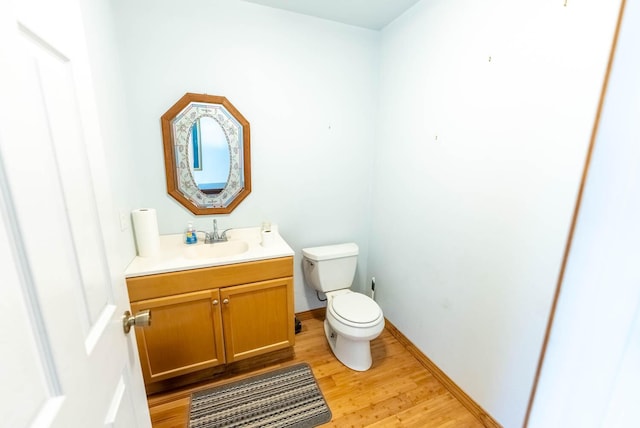 half bath featuring baseboards, wood finished floors, toilet, and vanity