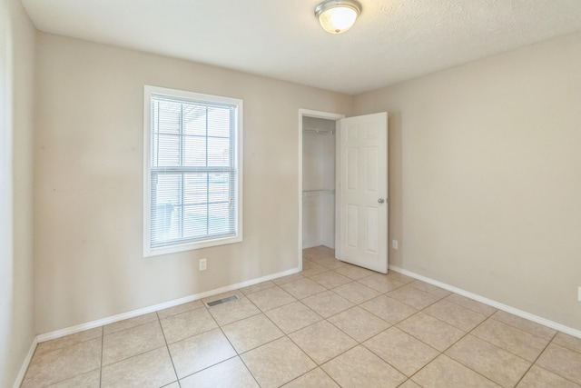 unfurnished bedroom with a textured ceiling, a closet, light tile patterned floors, and a walk in closet