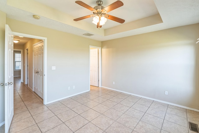 unfurnished room featuring a tray ceiling, light tile patterned floors, and ceiling fan