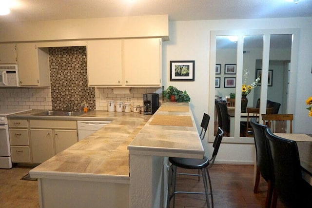 kitchen with backsplash, dark wood-type flooring, white appliances, and a breakfast bar