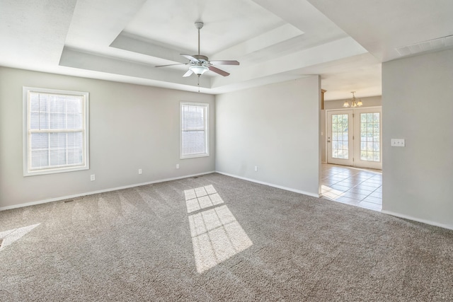 carpeted spare room featuring ceiling fan with notable chandelier, a raised ceiling, and a healthy amount of sunlight