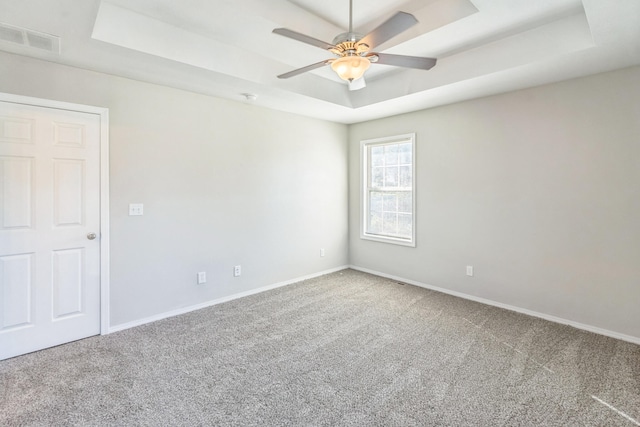 carpeted spare room with a raised ceiling and ceiling fan