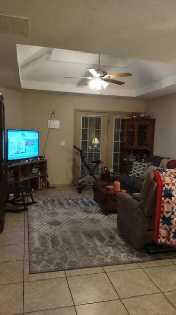 tiled living room featuring ceiling fan and a tray ceiling