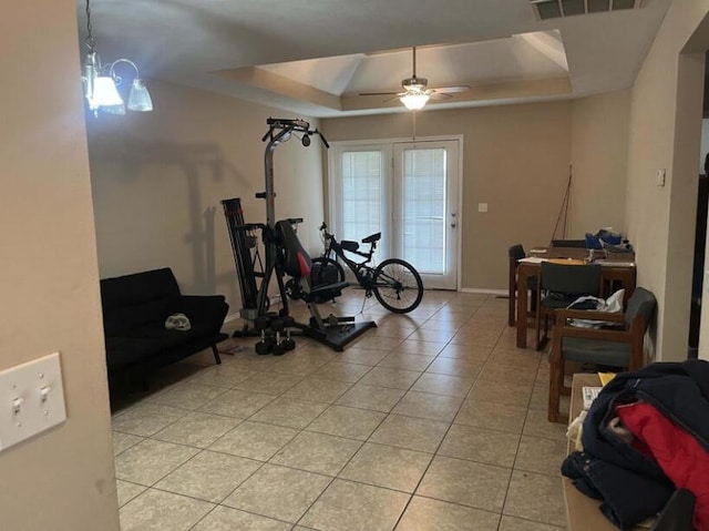 exercise area featuring a raised ceiling, light tile patterned floors, and ceiling fan