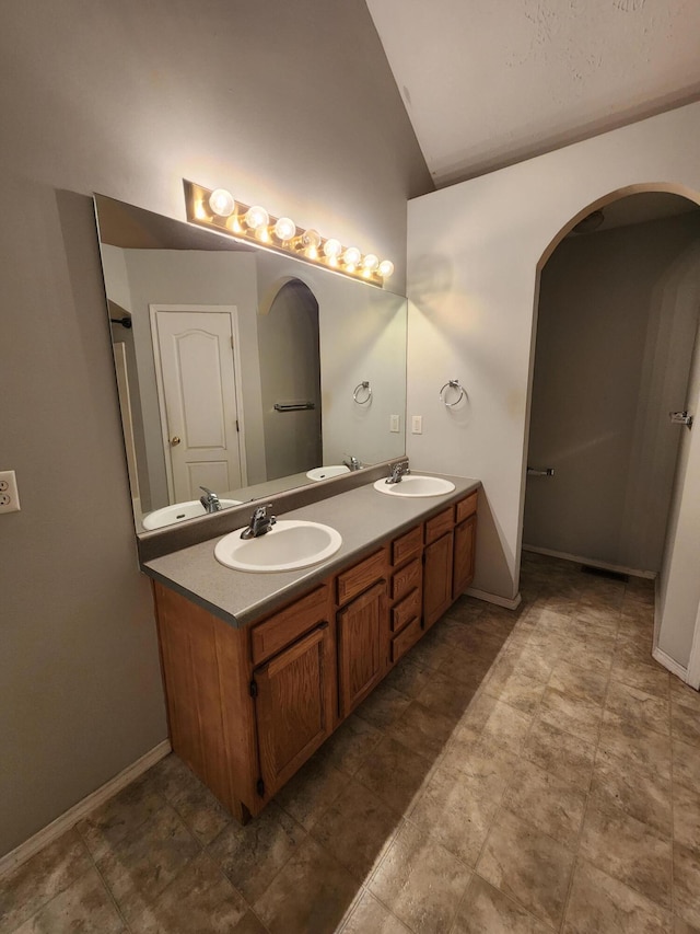 bathroom featuring baseboards, a sink, double vanity, and high vaulted ceiling