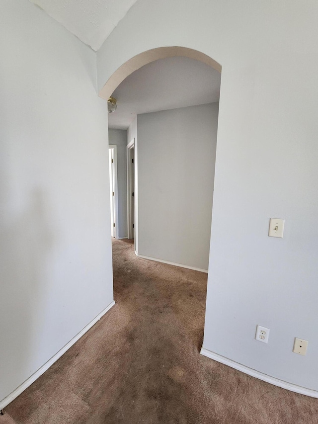 hall with carpet floors, baseboards, and arched walkways