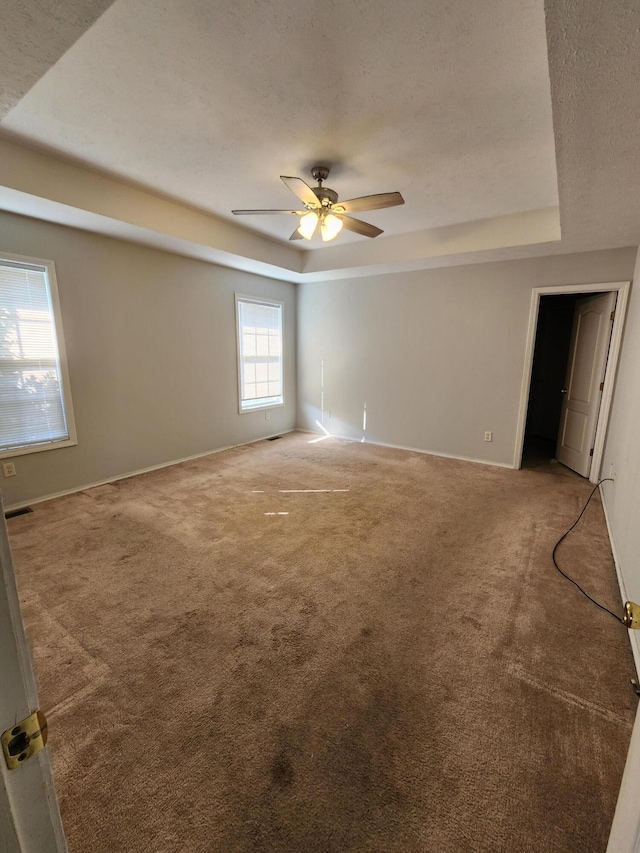 carpeted spare room featuring a tray ceiling, a textured ceiling, and ceiling fan