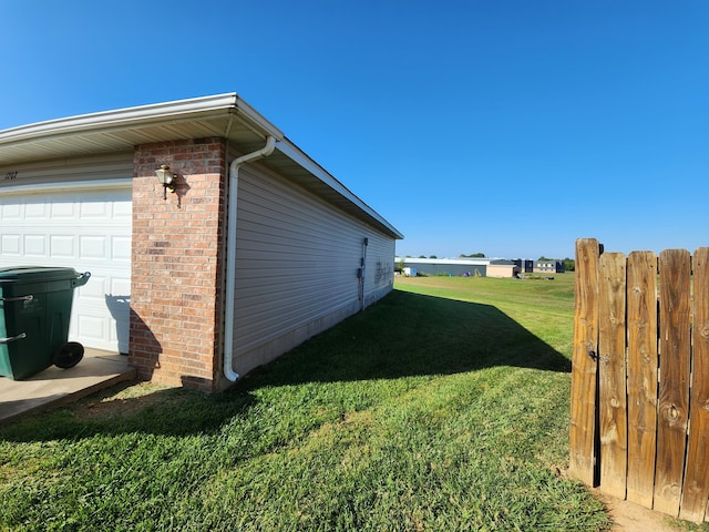 view of side of home featuring fence, a lawn, brick siding, and a garage
