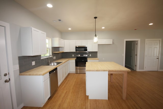 kitchen with pendant lighting, appliances with stainless steel finishes, white cabinetry, and butcher block counters