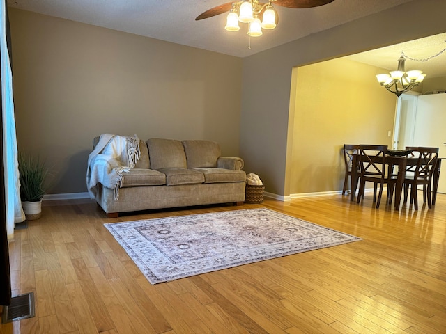 living room with ceiling fan with notable chandelier, light hardwood / wood-style floors, and a textured ceiling