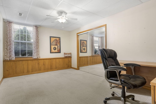 office space with light colored carpet, a wainscoted wall, wood walls, a ceiling fan, and visible vents