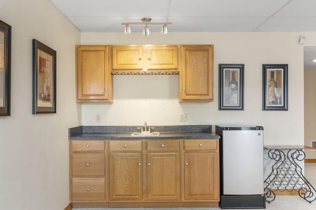 kitchen with dark countertops, freestanding refrigerator, a sink, and a paneled ceiling