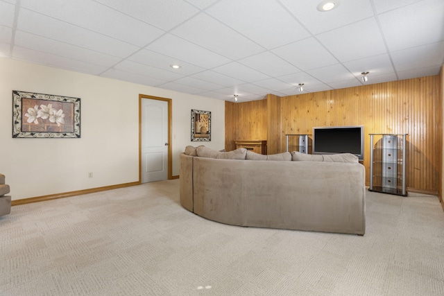 carpeted living room featuring a drop ceiling, wood walls, and baseboards