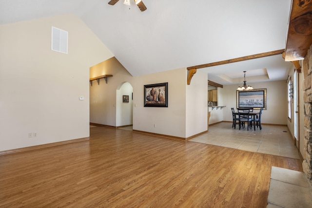 unfurnished living room featuring arched walkways, ceiling fan with notable chandelier, visible vents, baseboards, and light wood-style floors