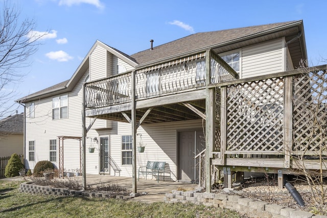 rear view of property featuring a shingled roof, a patio, and a deck