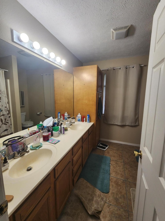 bathroom with vanity, toilet, a textured ceiling, and tile patterned floors