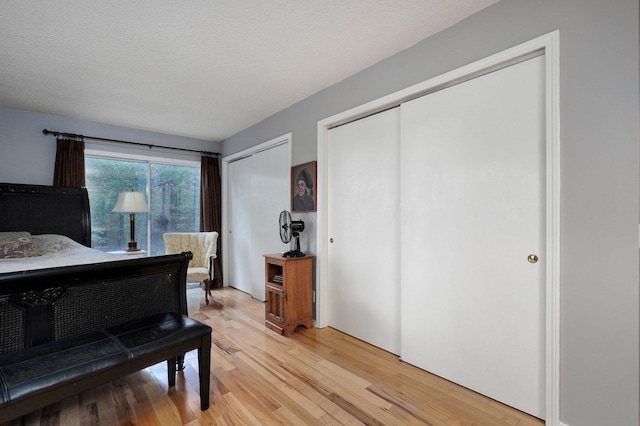 bedroom with multiple closets, a textured ceiling, and light wood-type flooring