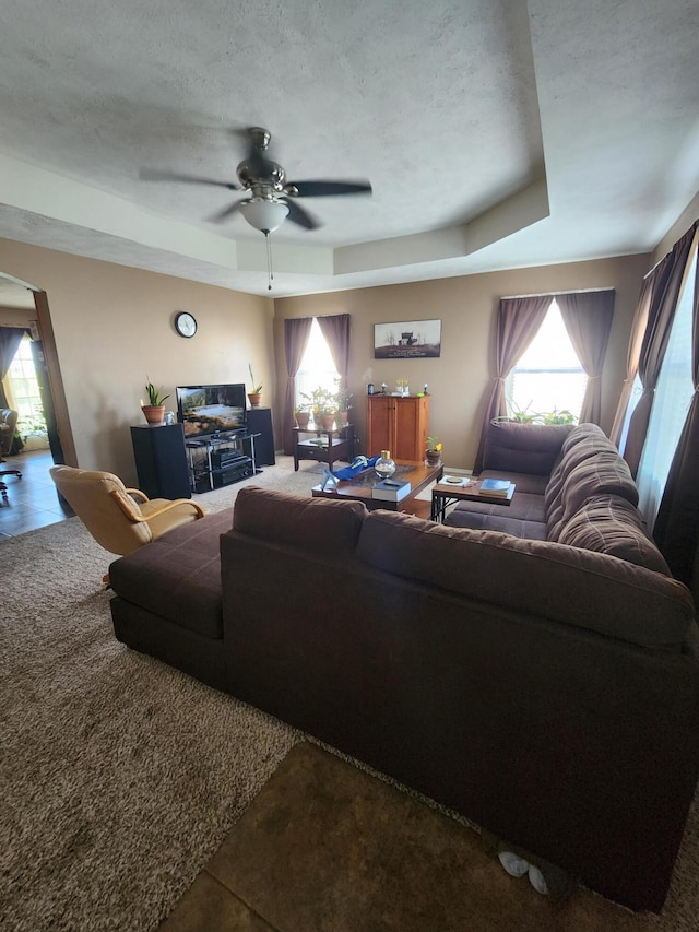 tiled living room featuring ceiling fan, a textured ceiling, and a raised ceiling