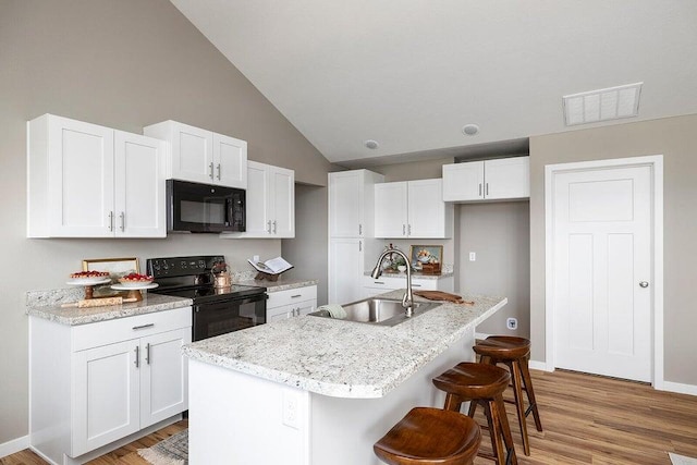 kitchen featuring light wood-type flooring, sink, an island with sink, white cabinets, and black appliances