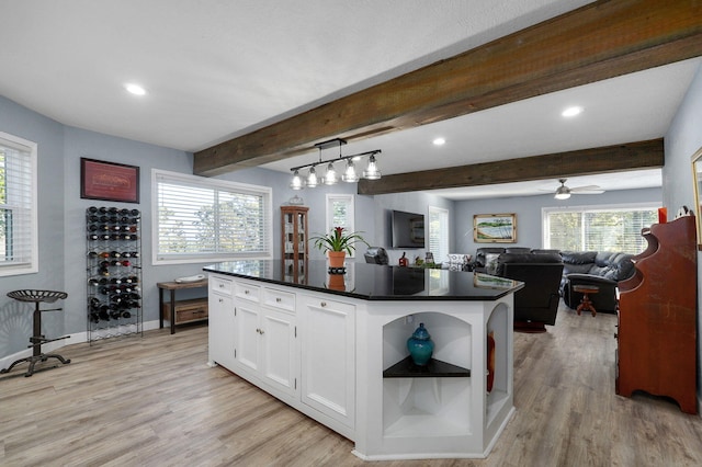 kitchen with hanging light fixtures, light hardwood / wood-style floors, white cabinets, a center island with sink, and beamed ceiling