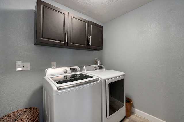 clothes washing area featuring cabinets, light wood-type flooring, a textured ceiling, and washing machine and clothes dryer