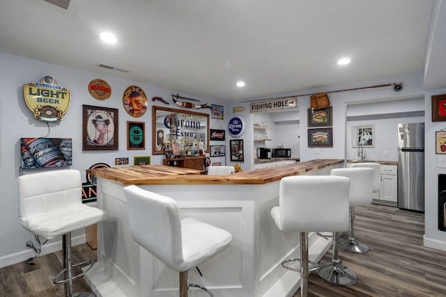 bar with butcher block countertops, hardwood / wood-style flooring, stainless steel fridge, and white cabinets