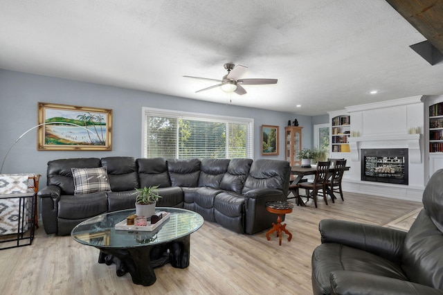 living room featuring ceiling fan, a textured ceiling, and light wood-type flooring