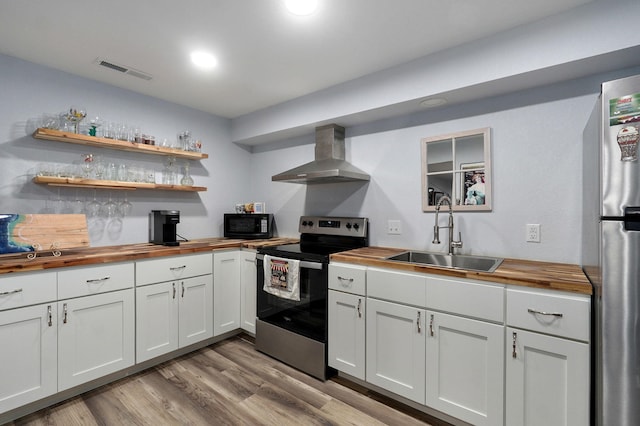 kitchen featuring sink, butcher block counters, white cabinets, stainless steel appliances, and wall chimney range hood